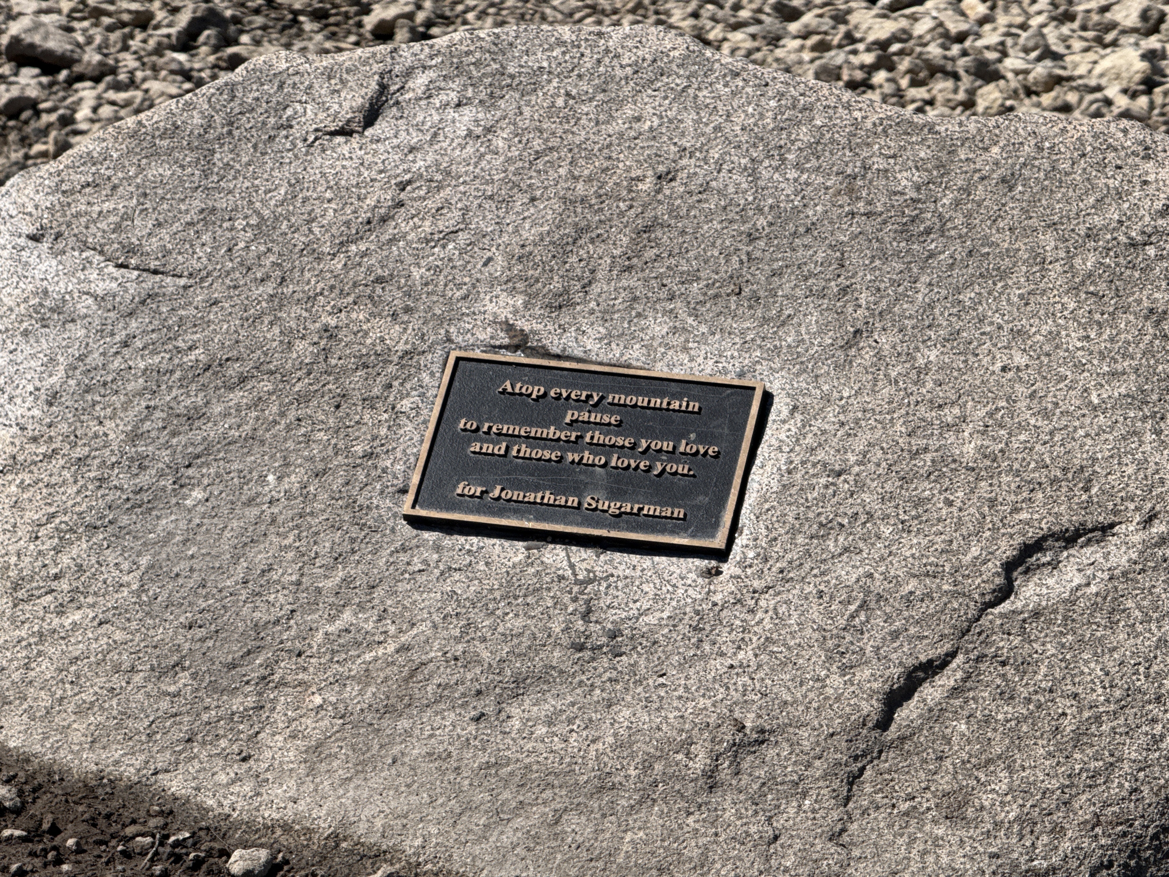 Bronze memorial plaque on summit rock reading: Atop every mountain pause to remember those you love and those who love you. For Jonathan Sugarman.